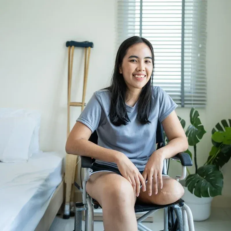 A Woman is Sitting in a Wheelchair and Smiling — Collis Care In Dundowran, QLD
