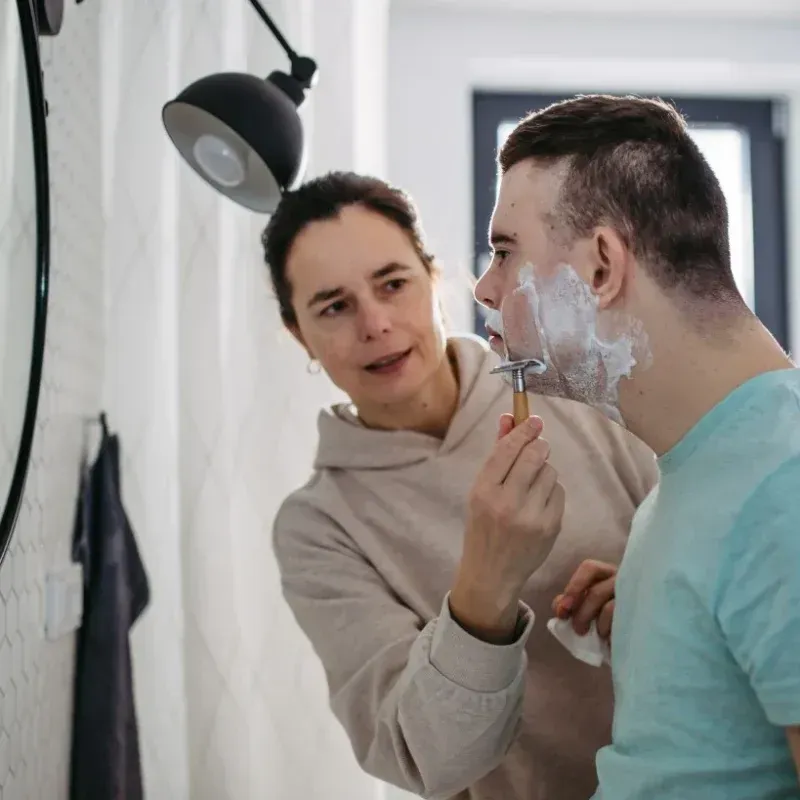 A Woman is Shaving a Man 's Face in Front of a Mirror — Collis Care In Dundowran, QLD