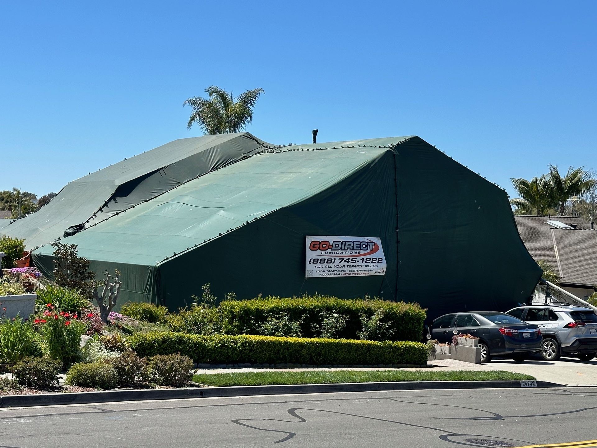 Green tent covering a building with a sign, cars parked in front, clear sky.