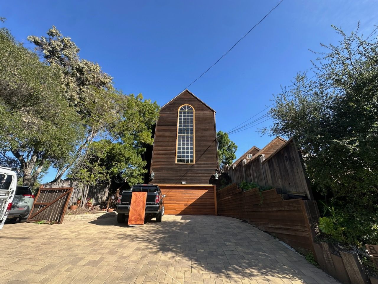 Wooden house with tall arched window, brown garage door, and a pickup truck parked in front.