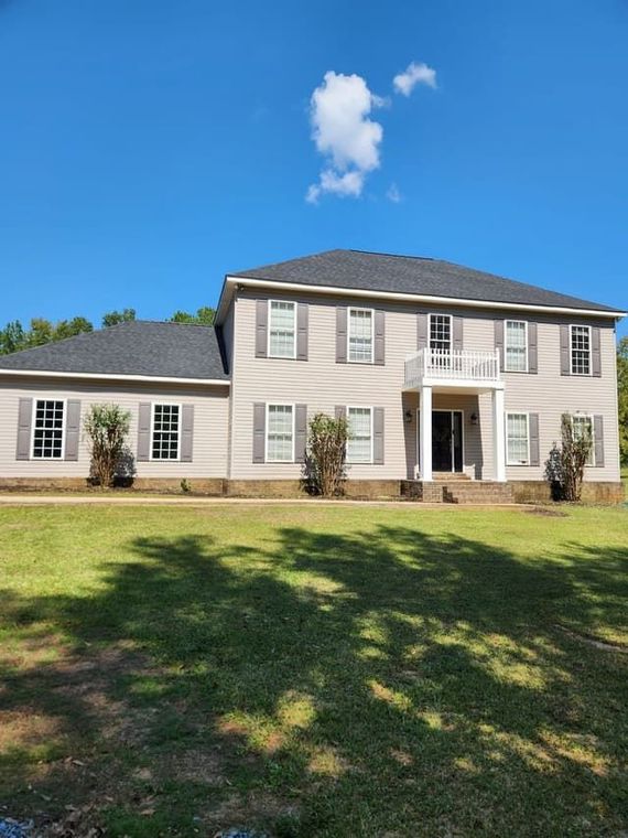 A large house with a lot of windows and shutters is sitting on top of a lush green field.