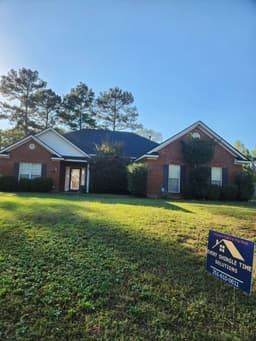 A brick house with a blue roof and a sign in front of it.
