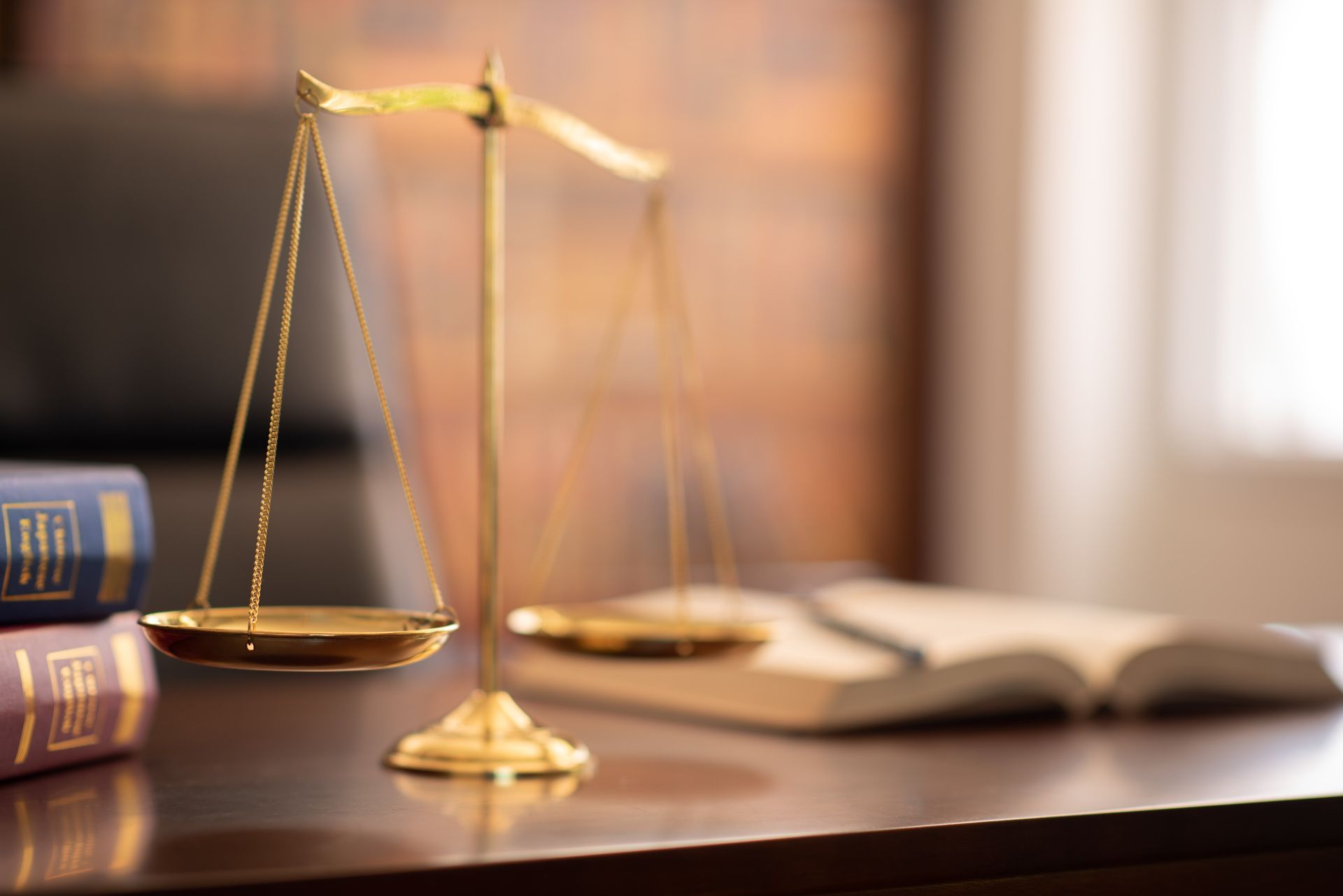 Gold scales of justice on a desk with law books and an open book in the background
