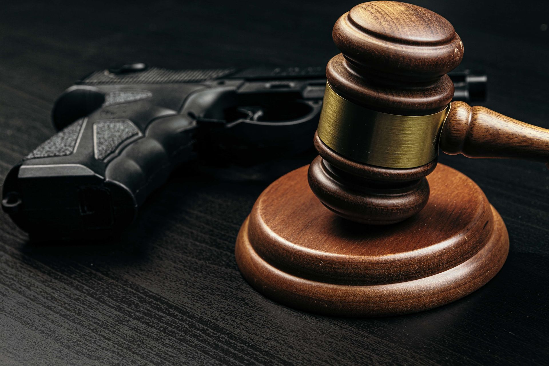 Wooden gavel beside a handgun on a dark surface, symbolizing law and crime.
