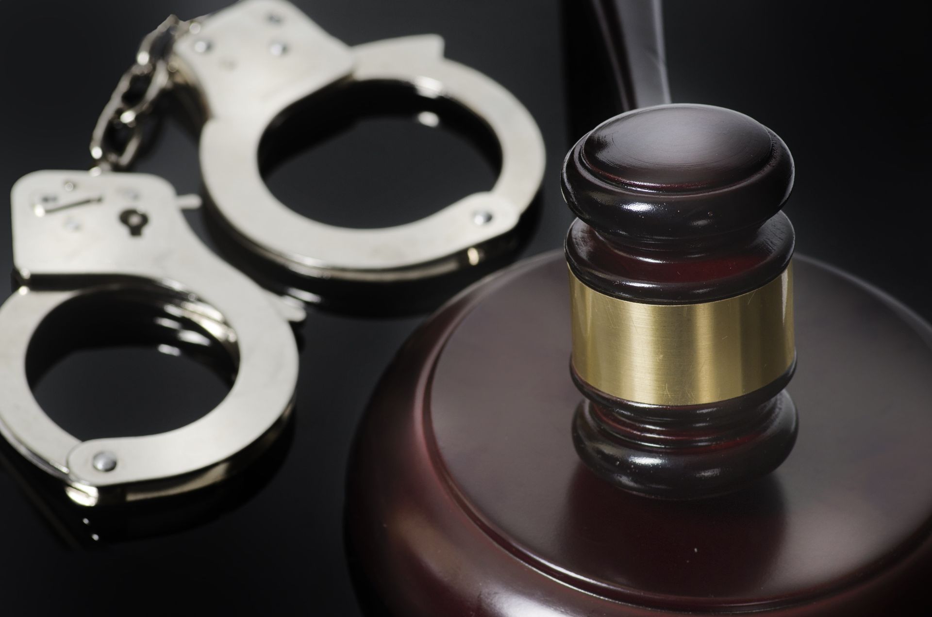 Handcuffs beside a judge’s gavel on a dark surface