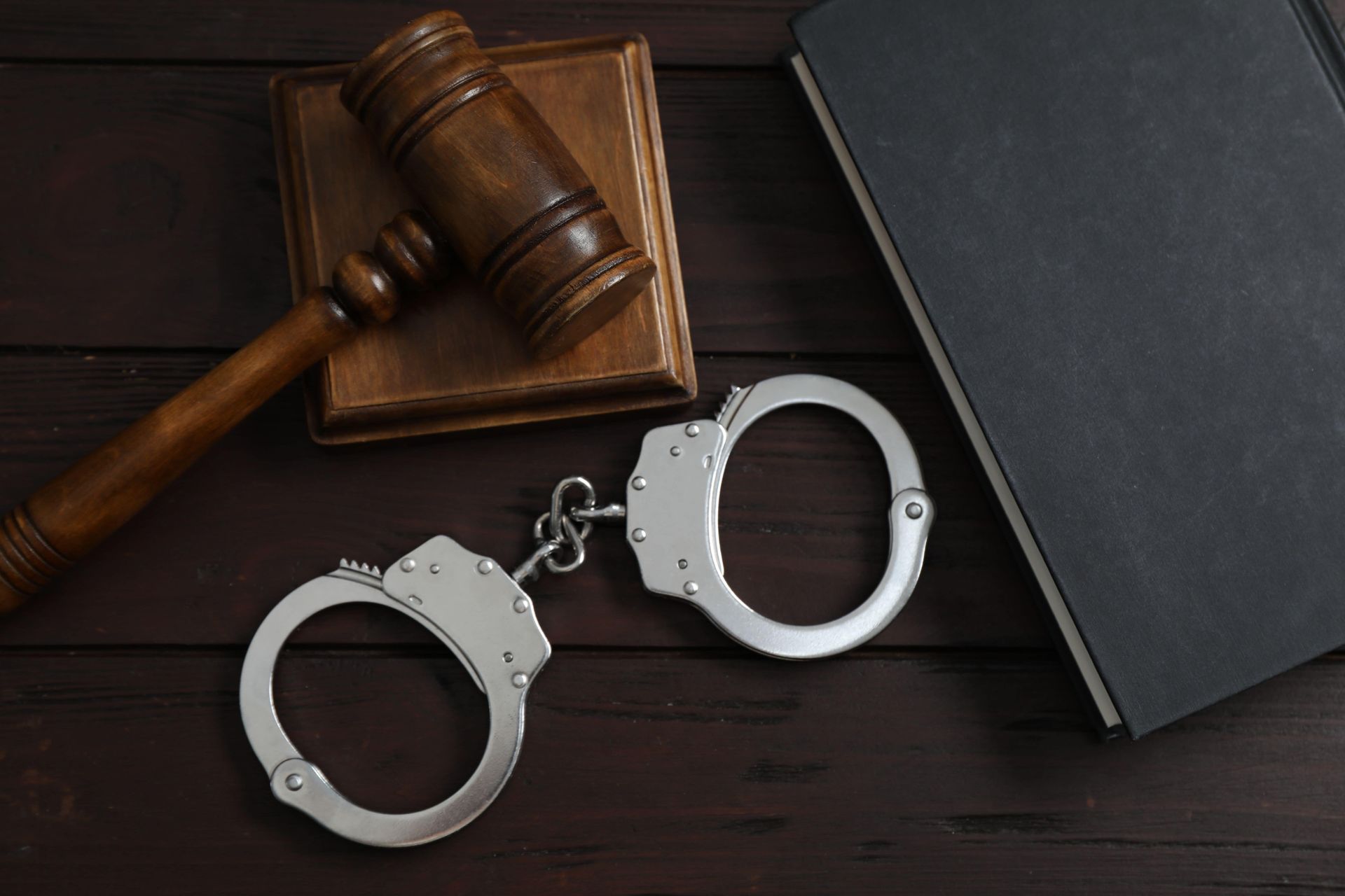 Handcuffs beside a judge’s gavel and law book on a dark desk