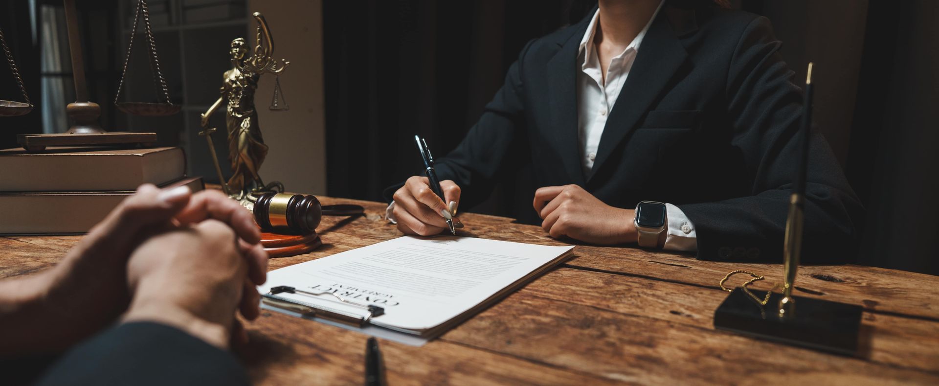 Business meeting at a wooden table, with people shaking hands across from a suited person taking notes.