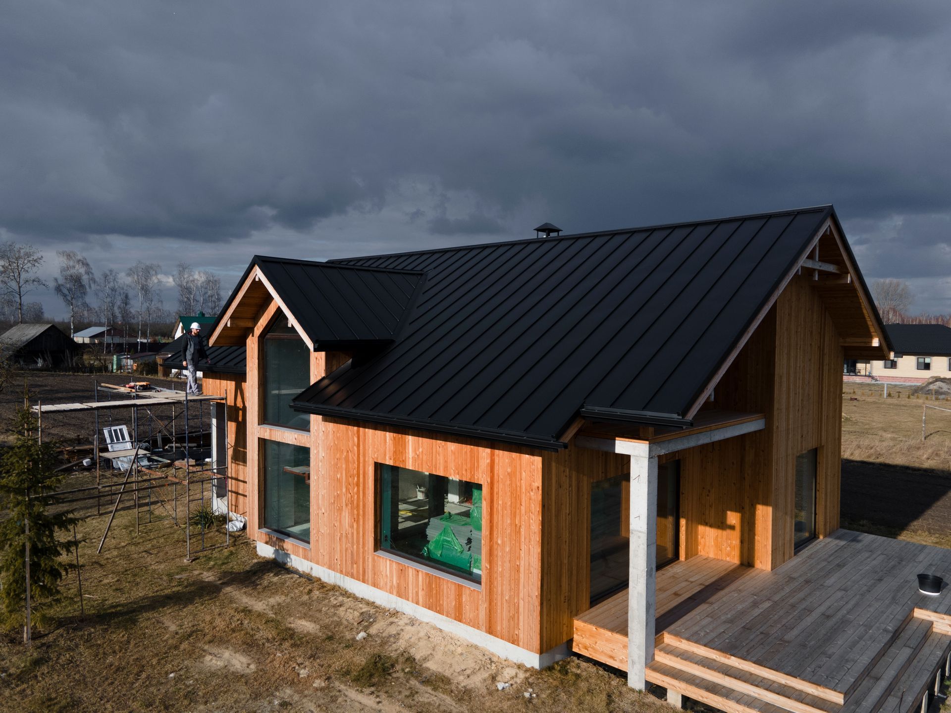 Wooden house with black roof under cloudy sky.