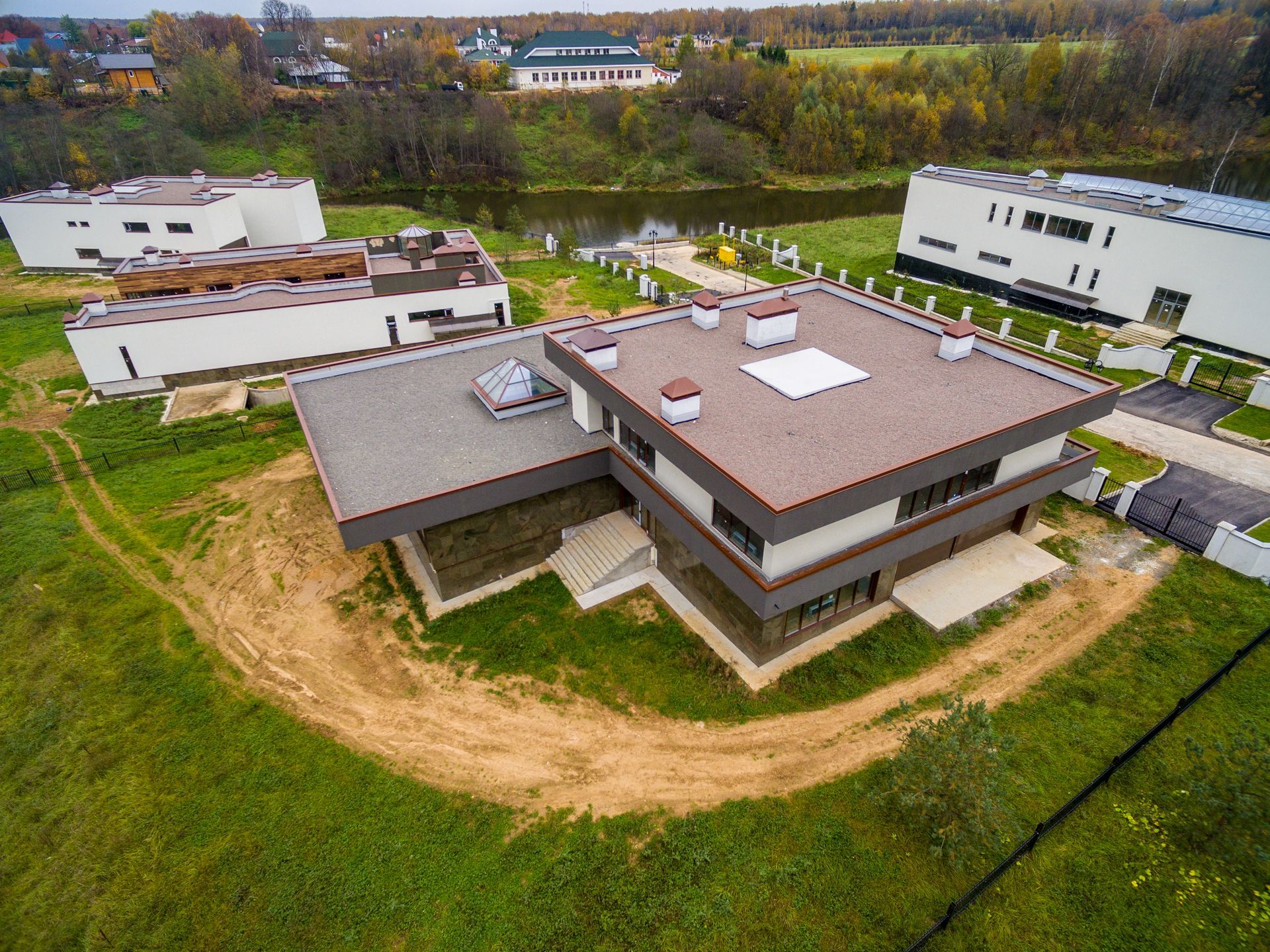Aerial view of modern houses with flat roofs on a green lawn, near a river.
