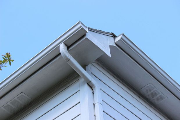 Corner of a white house with gutters and downspout against a blue sky.