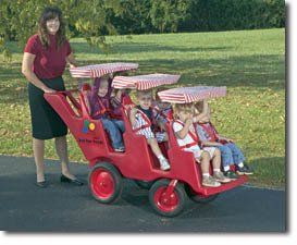 A woman is pushing a red wagon with four children in it.