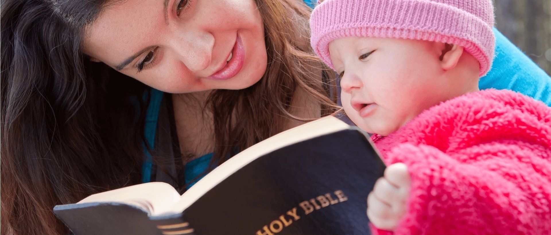 A woman is reading a bible to a baby.