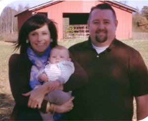 A man and woman holding a baby in front of a red barn