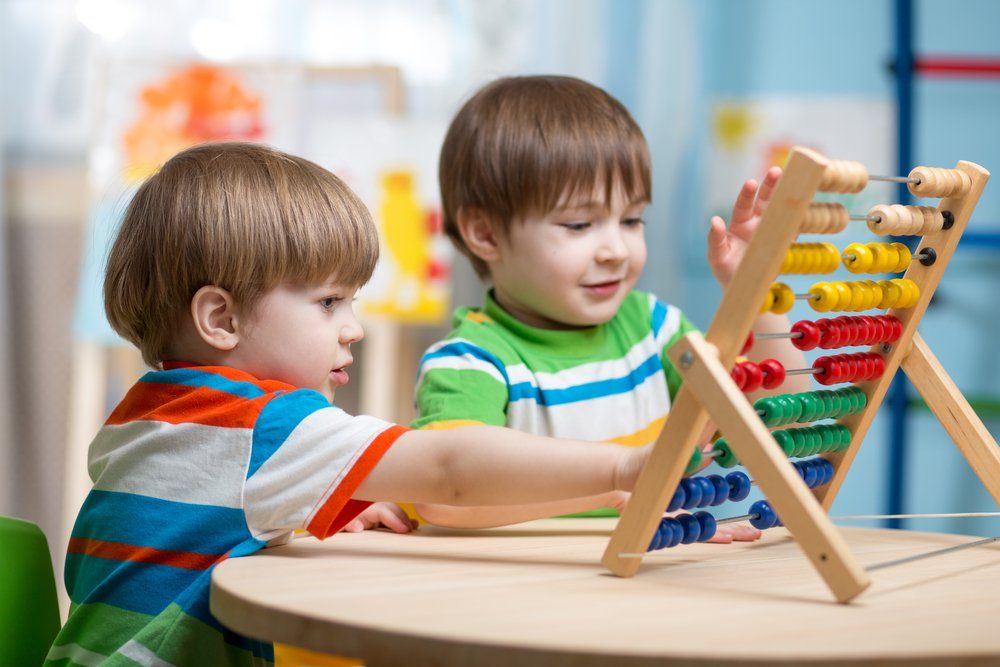 Two young boys are playing with an abacus at a table.