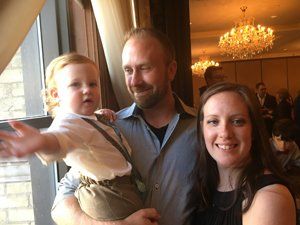 A man and a woman are holding a baby in front of a window.