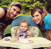 A man and woman are standing next to a baby in a high chair.