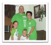 A family is posing for a picture in a living room wearing green shirts.