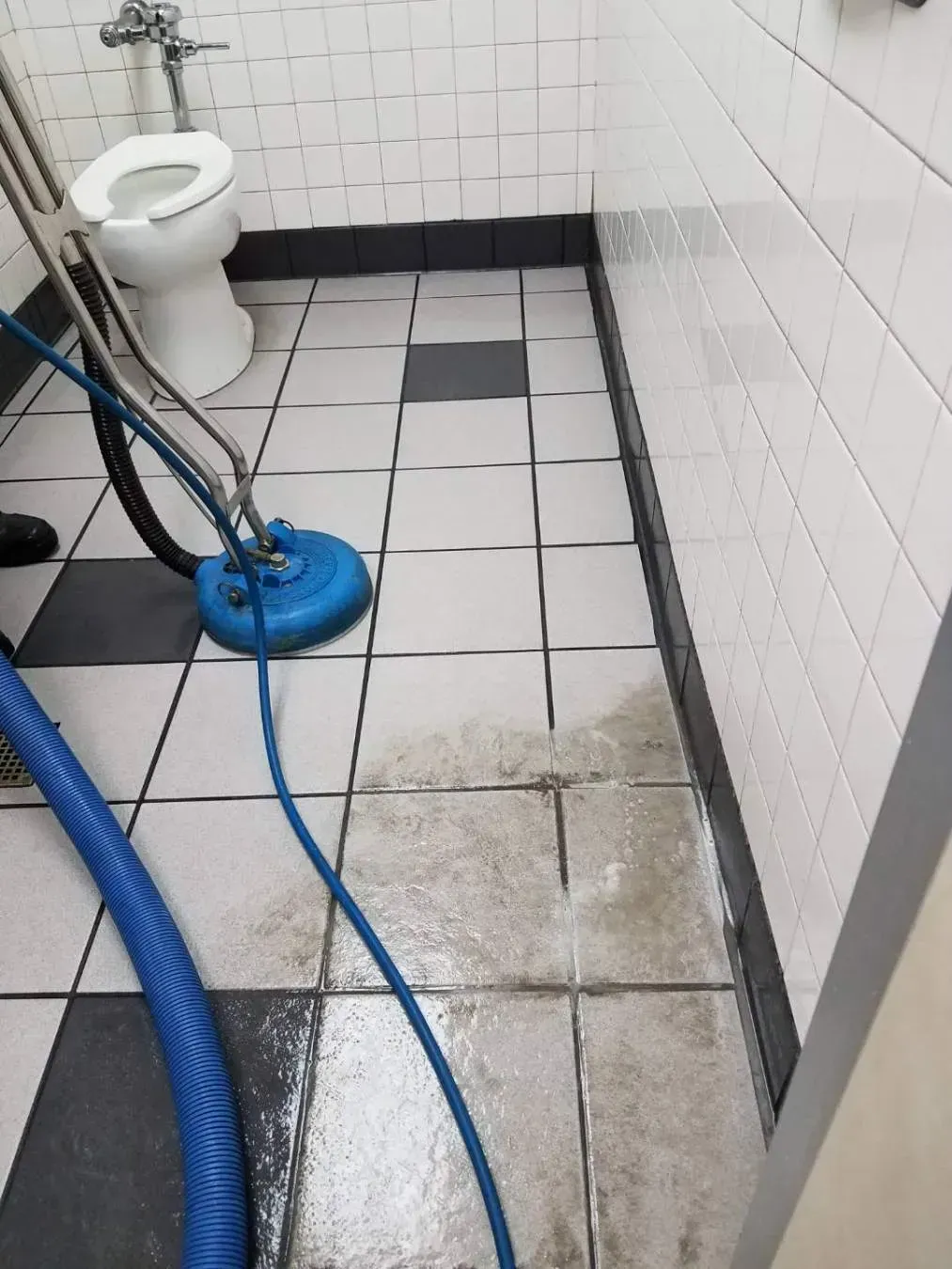 Bathroom floor cleaning with a blue power cleaner. Tile floor with toilet in background.