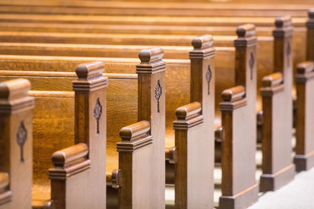 Rows of wooden church pews with decorative end pieces; neutral tones.