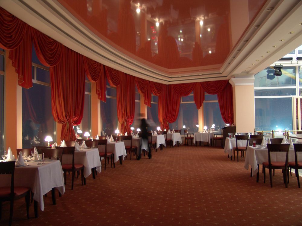 Restaurant interior with orange drapes, tables with white tablecloths, and a mirrored ceiling reflecting lights.