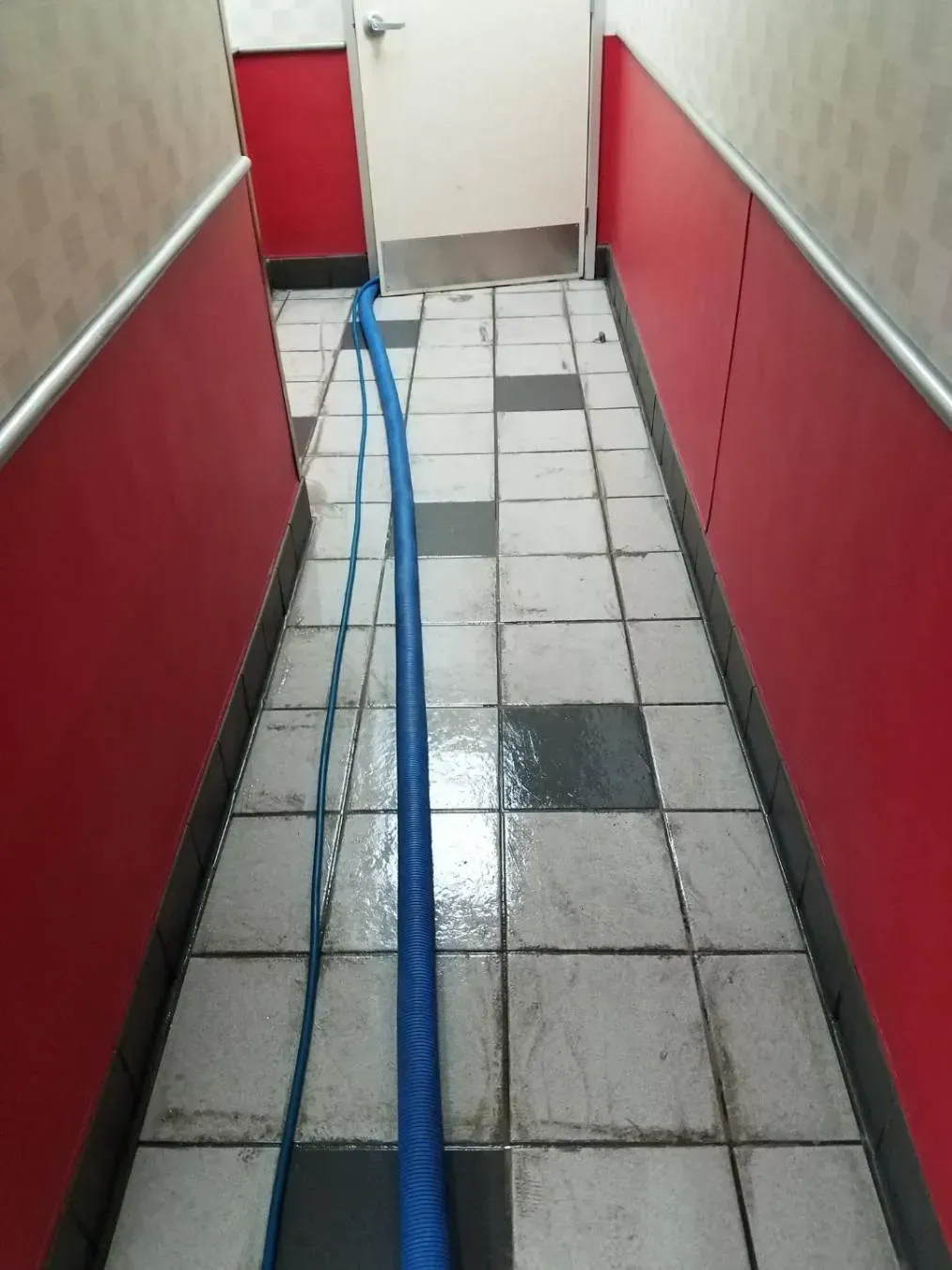 Narrow tiled hallway with a blue hose running down the center, red wainscoting on walls.