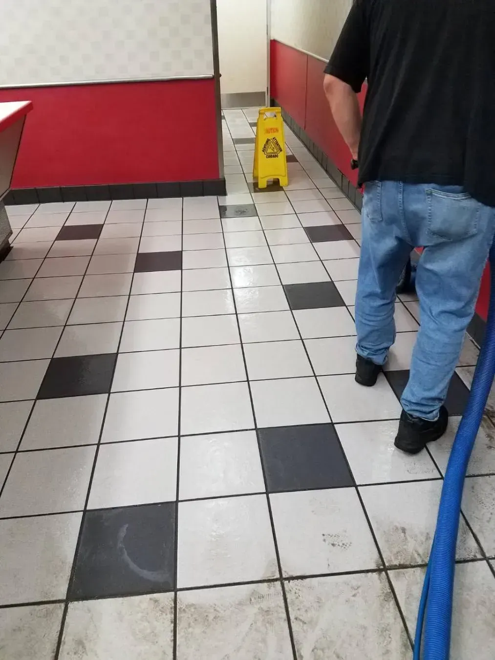 Person cleaning a tiled floor with a wet floor sign. Red and white walls.