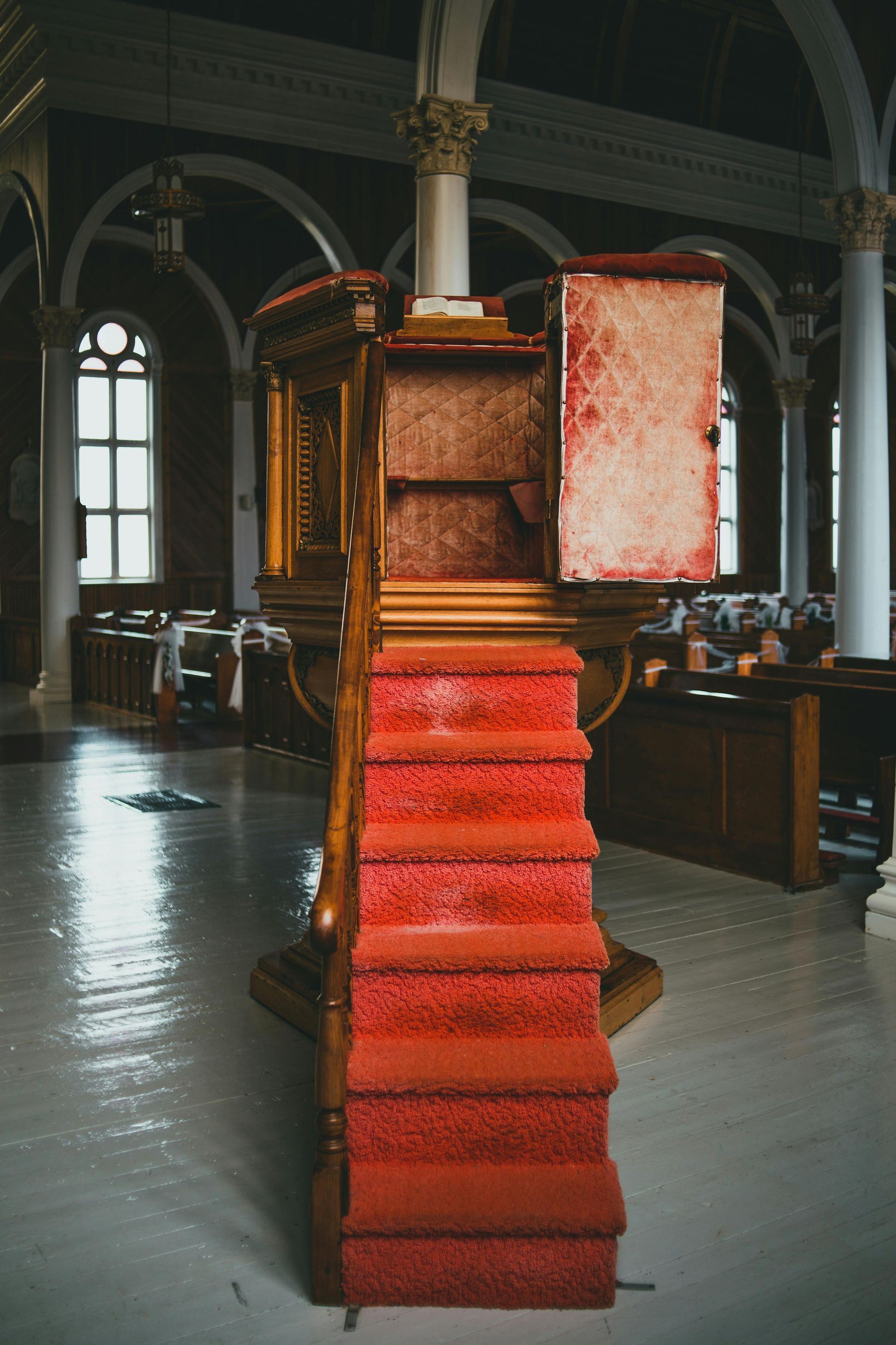 Wooden pulpit with red carpeted stairs, inside a church. Open door reveals empty shelves.