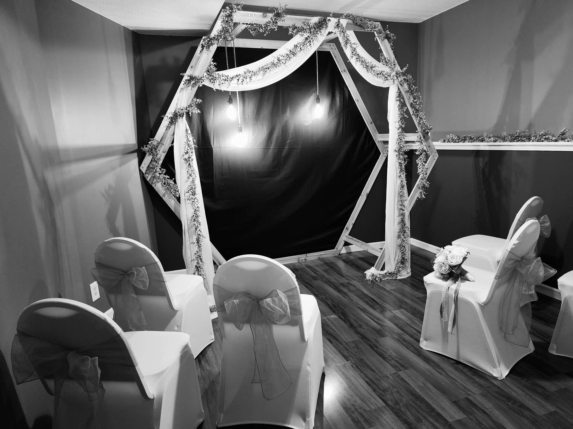 a black and white photo of a room with chairs and a wedding arch .