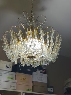 A gold chandelier with many crystal droplets hangs above boxes in a room. The light shines brightly from within the fixture.