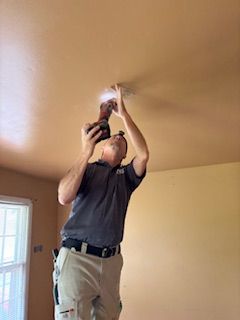 Man in khaki pants on a ladder, installing a light fixture on an orange-colored ceiling.