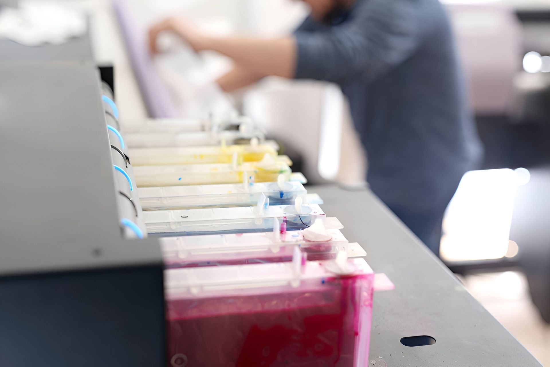 Ink Tanks of A Large Printer with A Blurred Person Filling Them in A Print Shop — Digi Print Pro in Bangalow, NSW