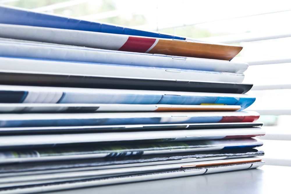 Stack of Colorful Magazines on A Desk, with A Window and Blinds in The Background — Digi Print Pro in Mullumbimby, NSW