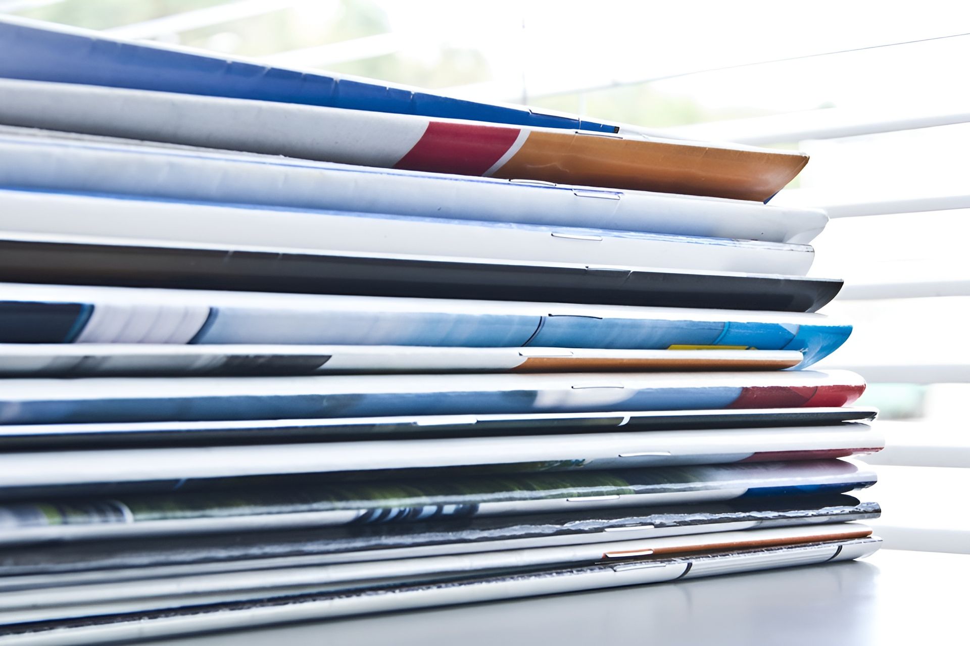 Stack of Colorful Magazines on A Window Sill, with A Blurred Background of Window Blinds — Digi Print Pro in Lismore, NSW