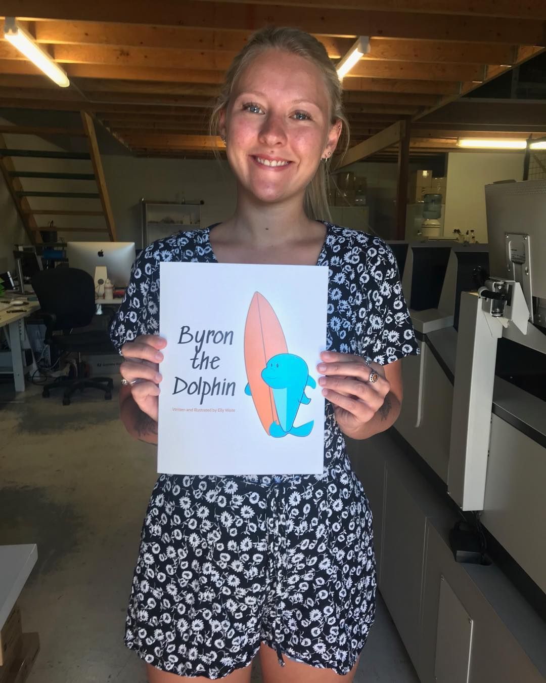 Woman Holding a Byron the Dolphin Book Cover in An Office with Printing Equipment — Digi Print Pro in Mullumbimby, NSW