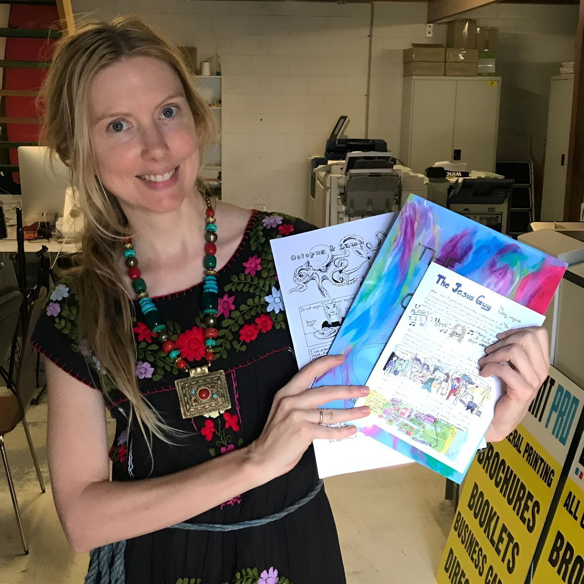 Woman Smiling, Holding Colorful Brochures and A Coloring Page, in A Printing Shop — Digi Print Pro in Byron Bay, NSW