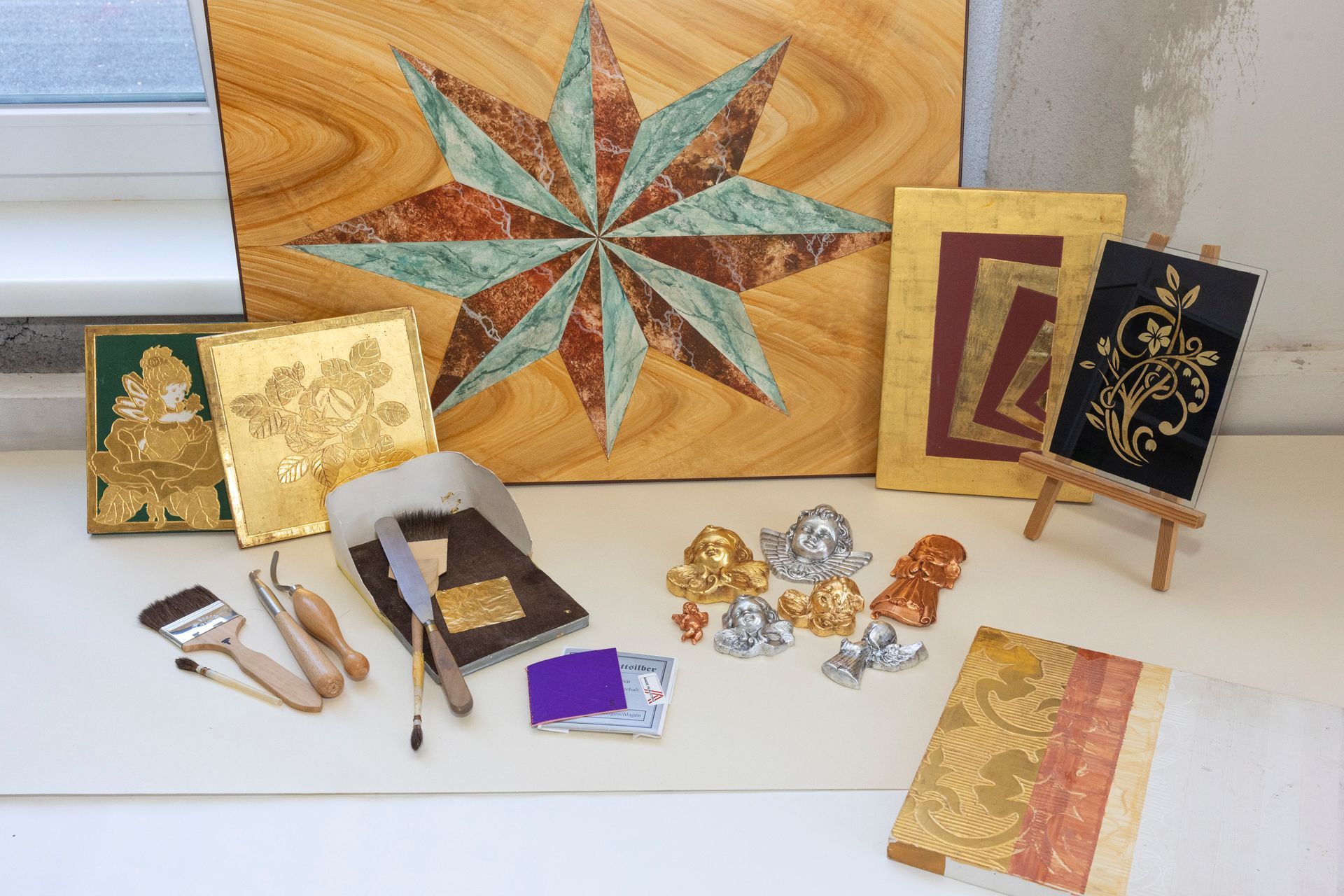 Künstlerbedarf und vergoldete Kunstwerke, darunter ein Sternenmotiv, Rahmen und Werkzeuge.
