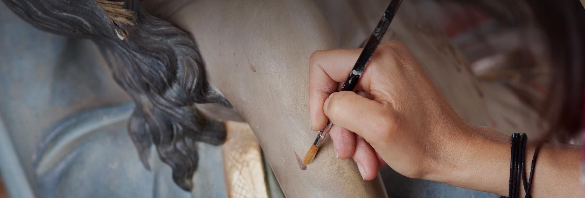 Eine Hand, die einen Pinsel hält, bessert eine bemalte Figur aus, wahrscheinlich eine Restaurierung.