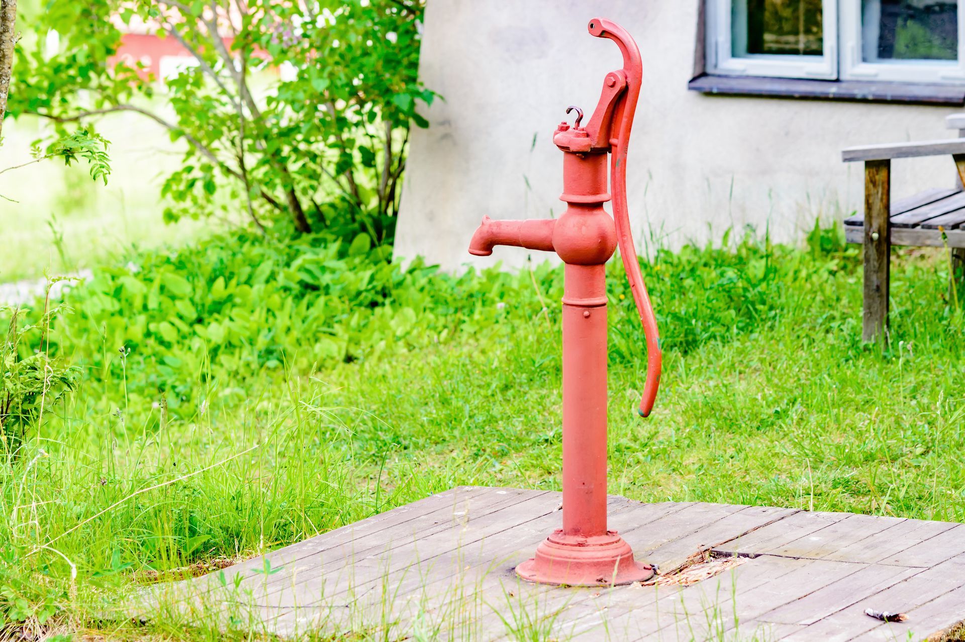 A red water pump is sitting on a wooden platform in front of a house.