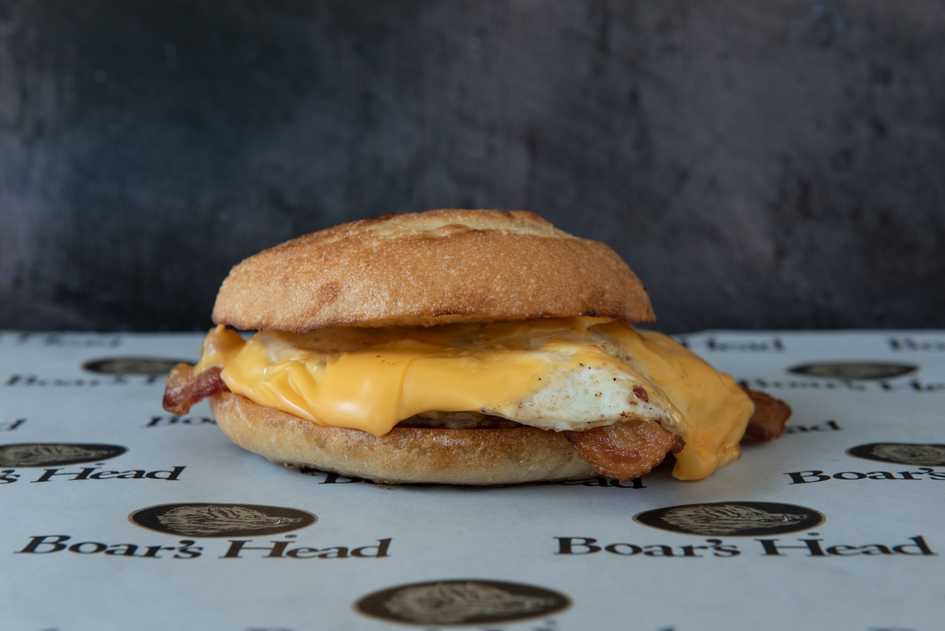 A sandwich with eggs , cheese and bacon on a bun on a table.