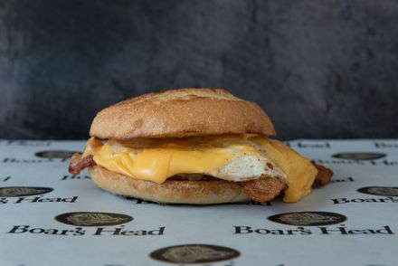 A sandwich with eggs , cheese and bacon on a bun on a table.