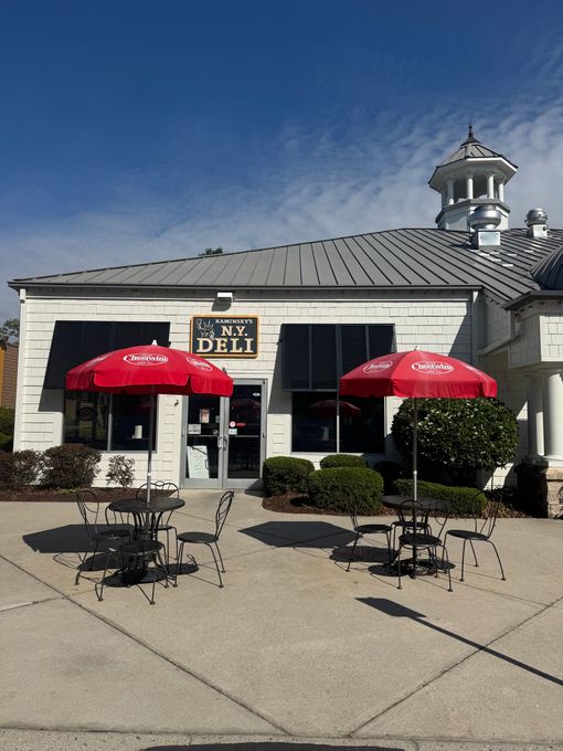 A deli with red umbrellas and tables outside