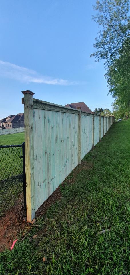 A wooden fence is sitting in the middle of a grassy field next to a chain link fence. Clarksville, TN