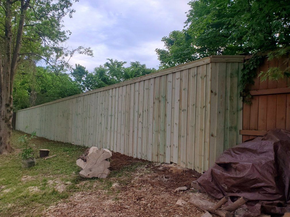 A long wooden fence is surrounded by trees in a yard.