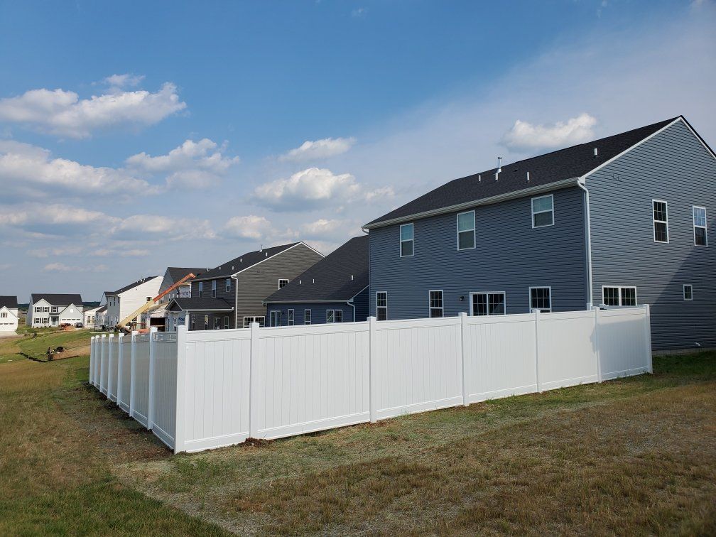 A white fence surrounds a large house in a residential area.