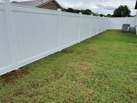 A white fence surrounds a lush green lawn in a backyard.