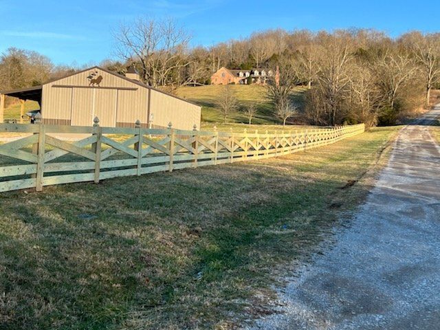 A wooden fence along a dirt road with a barn in the background.