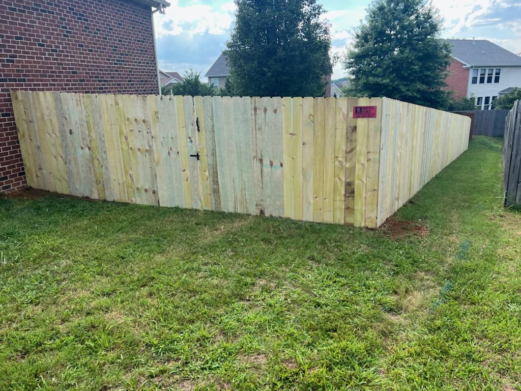 A wooden fence is sitting in the grass in front of a brick house.
