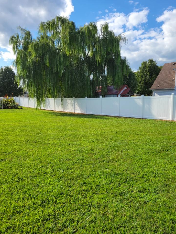 A white fence surrounds a large lush green field.