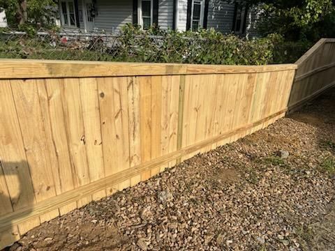 A wooden fence is sitting on top of a gravel driveway next to a house.