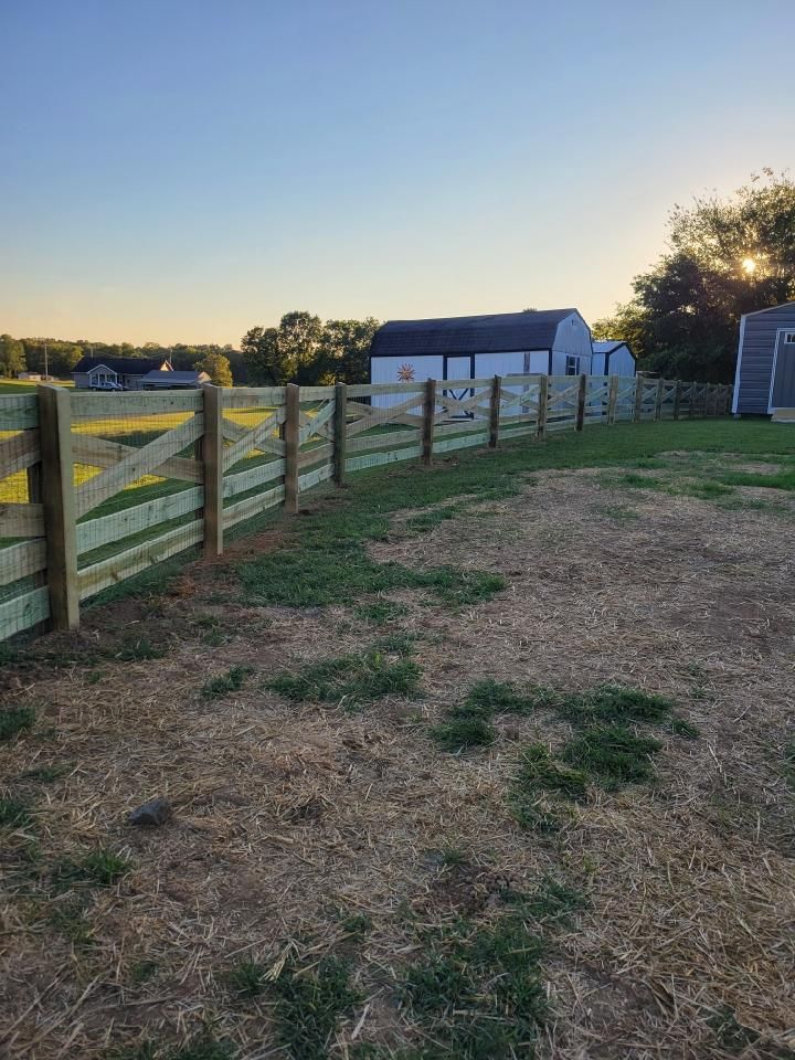 A wooden fence surrounds a grassy field with a barn in the background.
